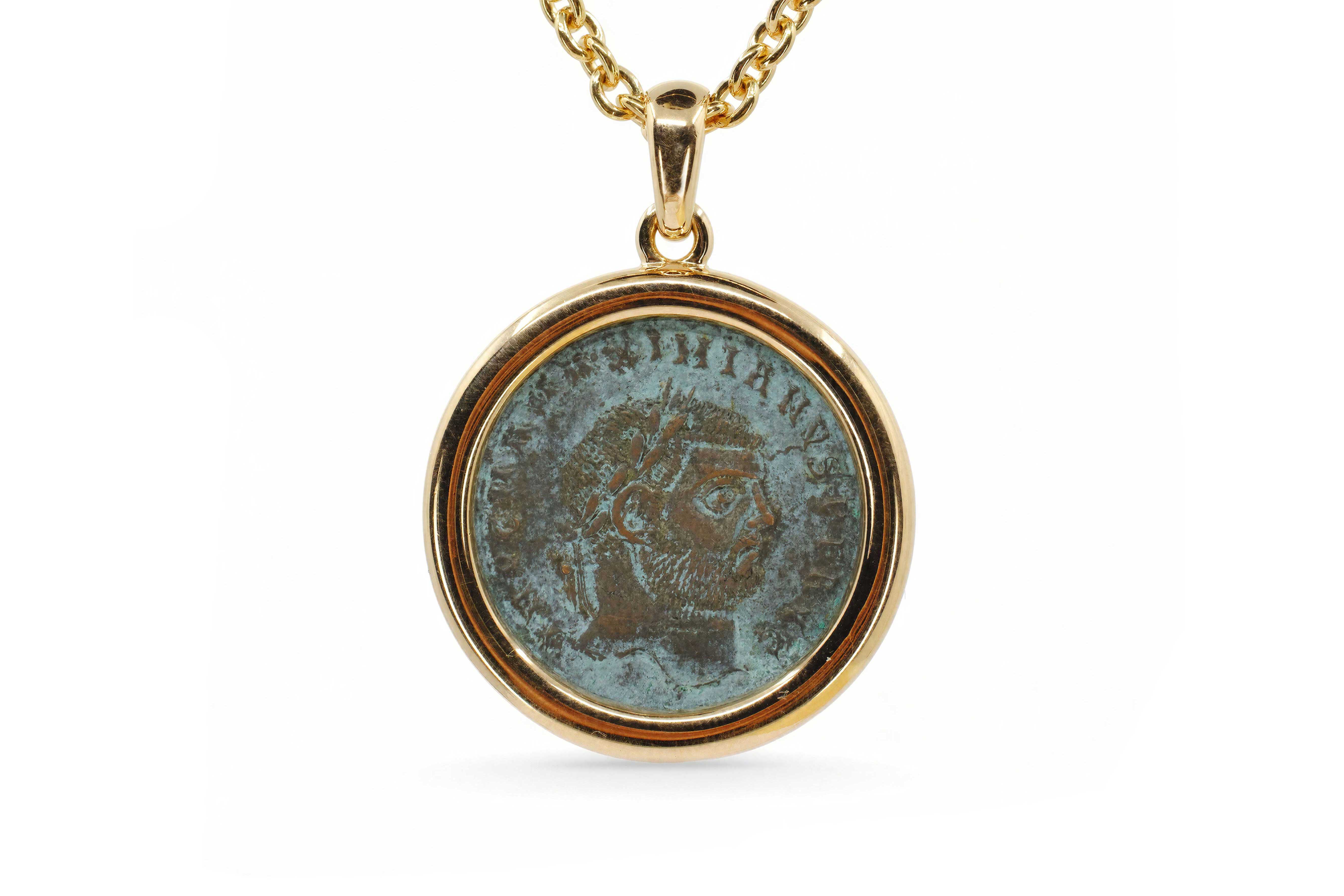 Close-up of a Bulgari Monete pendant: an ancient bronze Roman coin with a right-facing emperor's portrait and green-brown patina, set in a polished 18K yellow gold bezel on a rolo-link chain